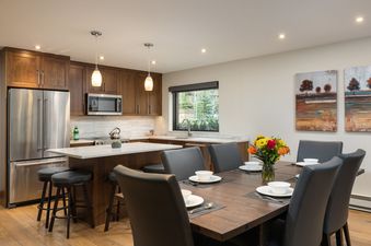 A modern kitchen and dining area with dark wood cabinets, stainless steel appliances, and a dining table set with white dishes and a colorful floral centerpiece.