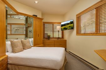 A cozy bedroom featuring a queen-sized bed, wooden furniture, and a wall-mounted flat-screen TV.