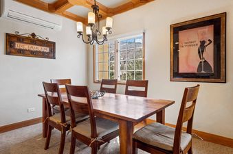 A rustic wooden dining table with six chairs and a chandelier above is shown, with a window showcasing a snowy mountain view.