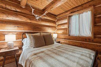 A serene bedroom at Apres Chalet with rustic log walls, a comfortable bed, and warm lighting.