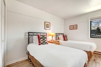 A cozy bedroom at Suncreek A7 featuring two twin beds with white linens and colorful geometric pillows, a wooden nightstand with a lamp, and framed artwork on the walls.