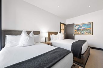 Two twin beds with white linens and gray throws, flanked by a shared nightstand and lamp, in the Solaris PHCE guest bedroom.