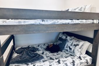 A cozy bunk bed in Arrow 213 features a quilt and pillows with a moose and tree pattern.