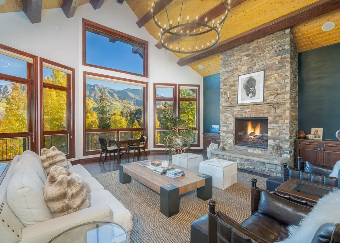 The spacious great room at Evergreen featuring a large stone fireplace, cozy seating, and large windows with mountain views.