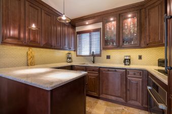 A U-shaped kitchen with dark wood cabinets, light granite countertops, and a yellow tiled backsplash, featuring modern appliances and a window above the sink.