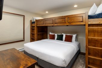 A comfortable bunk bed setup in a bedroom at Montaneros 317, featuring a double bed on the bottom and a single bunk on top, both made with white linens and accented with colorful pillows.