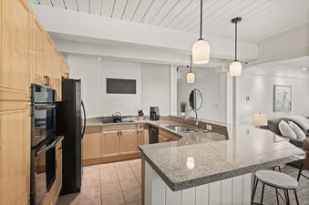 A modern kitchen in Enclave 209 with light wood cabinets, granite countertops, and stainless steel appliances.