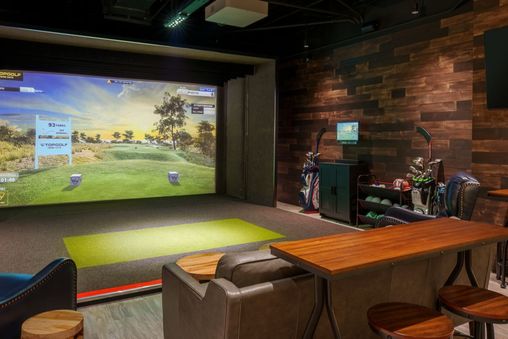 A Topgolf suite features a golf simulator, comfortable seating, and a flat-screen TV.