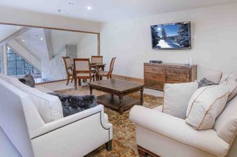 The living area of Vail Mountain View 402 features a large TV, a comfortable couch, a coffee table, a rug, and a view of the trees outside.