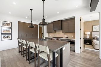 A modern kitchen with a large island and bar stools, leading into a cozy bedroom at The Ridge at Canyons Village.