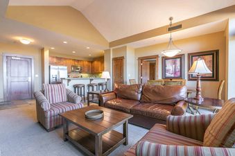 A living room with a large brown leather couch, striped armchairs, and a coffee table with a woven tray.