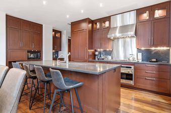 A modern kitchen with dark wood cabinets, stainless steel appliances, and a large island with gray bar stools.