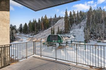 A private balcony at Founders Place 3103 overlooks a snowy ski slope with a ski lift and pine trees under a clear blue sky.