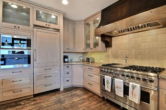 A modern kitchen with light wood cabinets, stainless steel appliances, a large range, and dark wood floors.