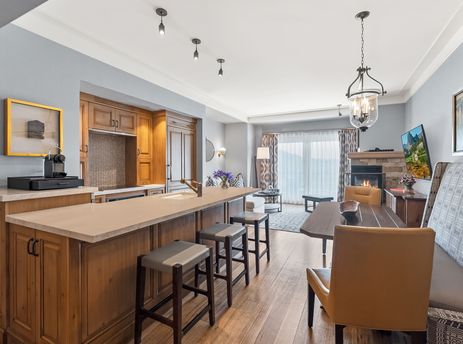 The open-concept living area of the St Regis Mountainside View Suite features a spacious kitchen island with bar seating, a dining table, and a comfortable lounge area with a fireplace.