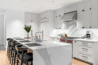 Modern kitchen with large marble waterfall island, black barstools, and high-end stainless steel Wolf appliances at Top Camp.