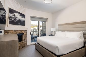 The bedroom in Moonlight Basin 16 Wildwood features a king-sized bed with plush bedding, a fireplace, and a balcony with views of the surrounding mountains.