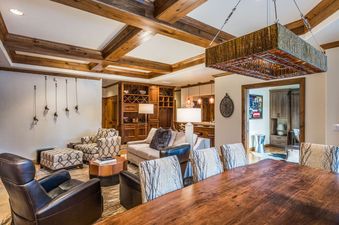 The Chateau Beaver Creek Residence 1304's open-concept living and dining areas feature exposed wooden beams, a large dining table, comfortable seating, and a built-in bar.
