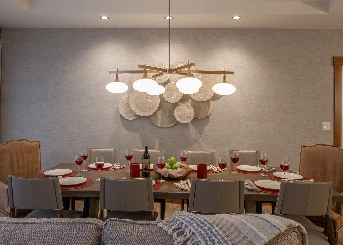 A formal dining area with a large wooden table set with plates, wine glasses, and a decorative centerpiece, illuminated by a modern chandelier.