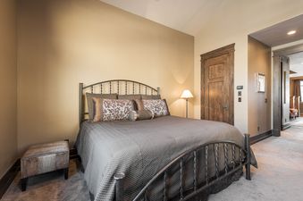 The bedroom at Harmony Haus features a dark metal bed with patterned pillows, a floor lamp, and a wooden door with detailed molding.