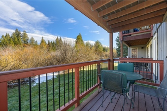 The image features a spacious balcony furnished with a table and chairs, offering a scenic view of a vast expanse of lush trees and majestic mountains in the distance.
