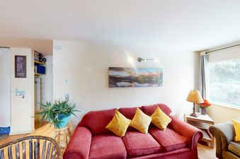 The living room of Beaver Creek Basecamp features a comfortable red couch with pillows, a wooden coffee table, and a lamp.