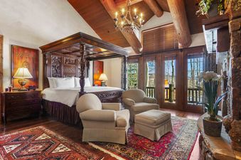 A cozy bedroom with a four-poster bed, two armchairs, and a fireplace.