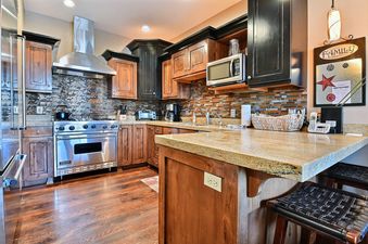 A modern kitchen with stainless steel appliances, wood cabinetry, granite countertops, and a mosaic tile backsplash.