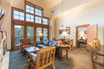 A spacious living room with a fireplace, a large window with a view of the snowy trees, and a comfortable sofa.