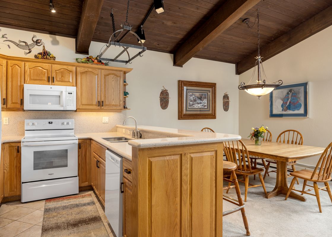 A cozy kitchen and dining area with wooden cabinetry, white appliances, a wooden dining table with chairs, and decorative artwork on the walls.