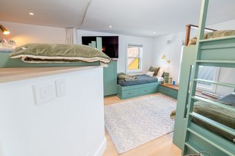 A bedroom with a built-in bunk bed with green frames and a light blue rug.