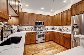 A fully equipped kitchen with wooden cabinets, stainless steel appliances, white marble countertops, and a stone backsplash at Bear Paw Lodge 2 Bedroom.