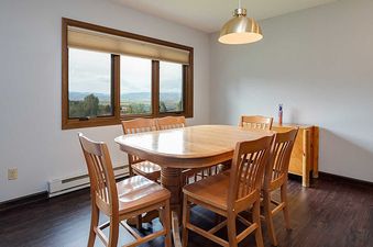 A bright dining area at Ranch at Steamboat RA309 featuring a wooden dining table and chairs, with a large window showcasing a panoramic view of hills and mountains.
