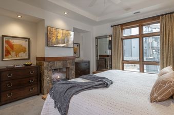 The primary bedroom at Buck Mountain 3 Bedroom One Steamboat Place 307 features a bed, stone fireplace with a TV above it, dressers, and a large window.
