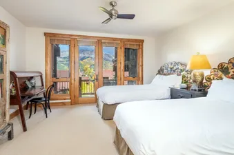 A bright bedroom at TRISTANT 115 with two twin beds, a wooden desk, and a balcony with a mountain view.