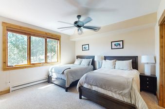 Two beds with white linens and gray blankets in a bedroom with a ceiling fan and a window.