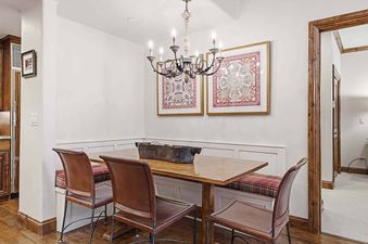 A cozy dining area at The Charter G230 features a long wooden table, built-in banquette seating with patterned cushions, and two leather chairs.