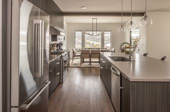 A modern kitchen and dining area in Beaverhead Condo 301 features stainless steel appliances, dark wood cabinetry, and a dining table with chairs, all illuminated by sleek light fixtures.