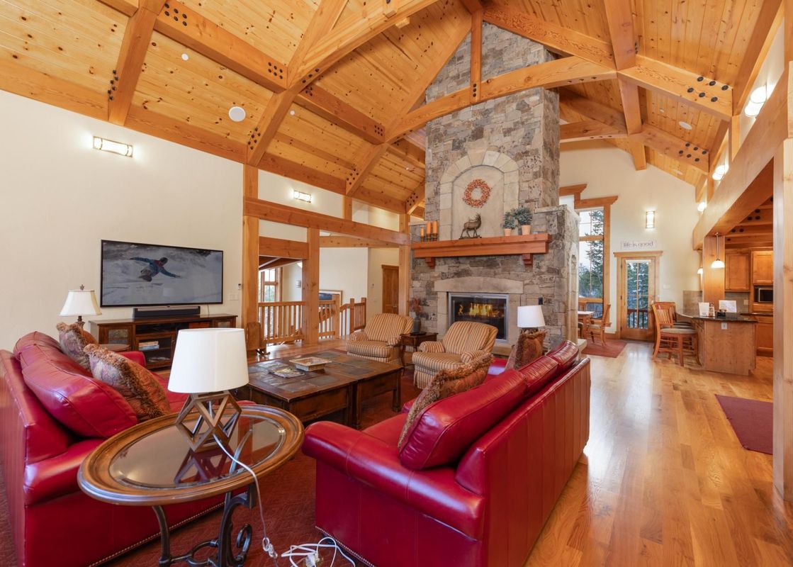 The living area of Timber Trail Lodge features a large stone fireplace, red leather sofas, and a high vaulted wooden ceiling, creating a cozy and luxurious atmosphere.