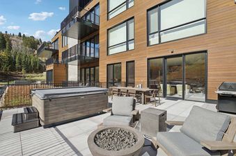 A spacious outdoor patio at Founders Place 2303 features a hot tub, fire pit, dining area, and barbecue grill, surrounded by mountain views.