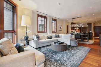 A spacious and inviting living area at Solaris 4EE features a comfortable white sectional sofa, a round coffee table, and a large patterned rug, with a modern kitchen and dining area visible in the background.