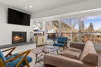 Durant Condominiums Unit D4 features a living room with a fireplace, a leather sofa, and a view of the snowy mountains.