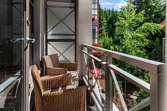 The balcony of The Westin Resort Deluxe Studio Suite with 2 Queen Beds features two wicker chairs and a glass railing overlooking a lush forest.