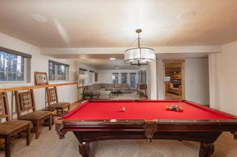 A spacious recreation room at Sawmill Run Lodge features a large red-felted pool table in the foreground, with comfortable seating and additional living areas visible through wide archways.
