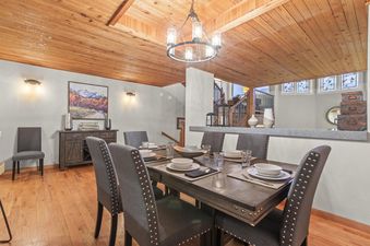 The elegant dining room at Motherlode 3, featuring a wooden ceiling, hardwood floors, a chandelier, and a dark wood dining table with upholstered chairs.