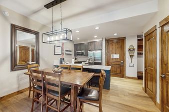 A dining room with a wooden table and chairs, a light fixture above, and a large mirror on the wall.