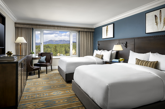 A hotel room with two beds and a view of mountains and trees from a large window.