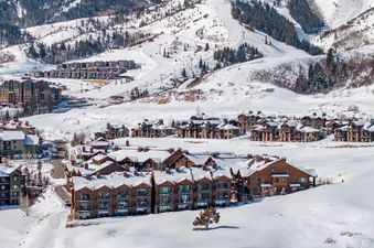 A luxury ski-in/ski-out unit, Juniper 901, in a snow-covered mountainous landscape with ski slopes and other buildings.