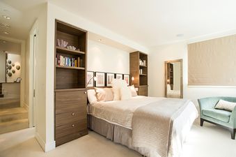 A bedroom with a large bed, white bedding, and a fluffy white throw blanket. There are two built-in bookshelves and a mirror on the wall.