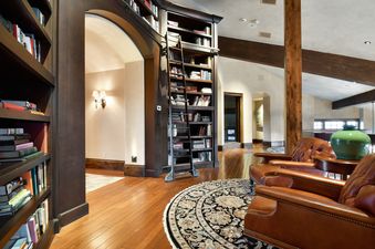 A library at Ski Dream Home features dark wood bookshelves, a rolling ladder, a circular area rug, and two brown leather armchairs.